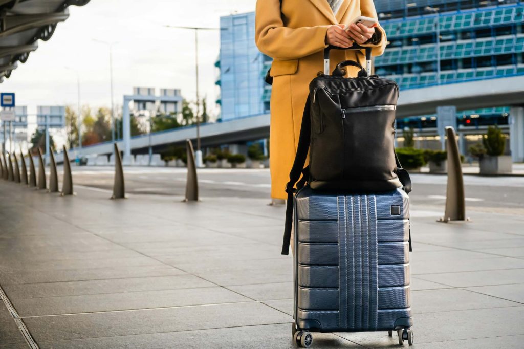 Woman traveler in coat with handbag and suitcase orders taxi.jpg